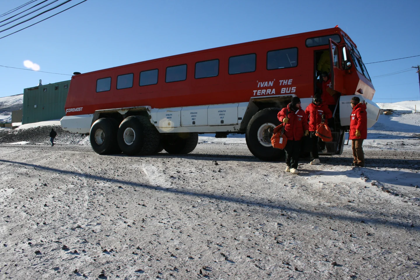 Large red Antarctic passenger bus outside a McMurdo station building