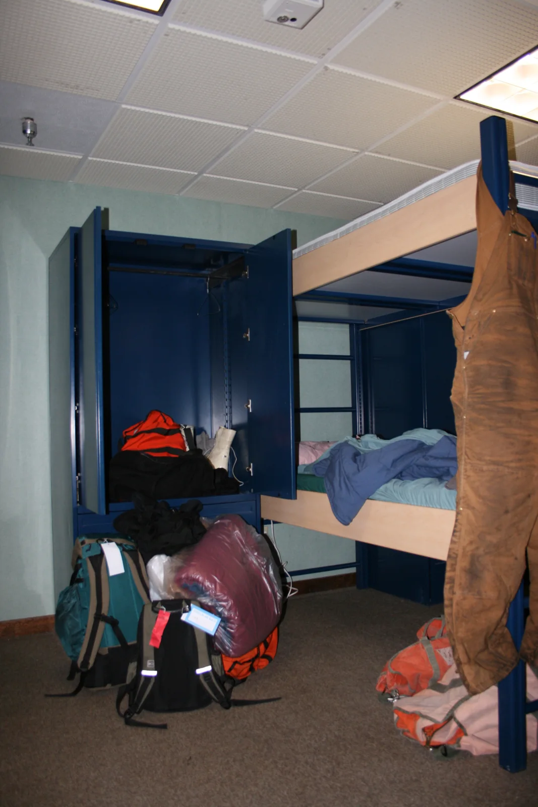 Bunk beds, coats, luggage and an open door inside a small McMurdo dormitory room