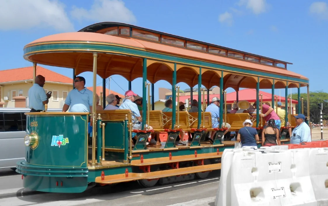 Passengers aboard the green and yellow open-sided Oranjestad streetcar 1265