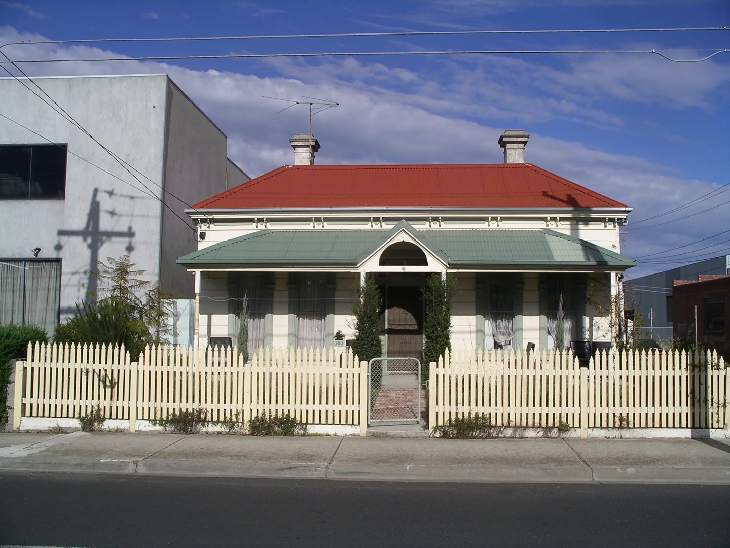 A Brunswick cottage with a red roof, veranda and pale picket fence