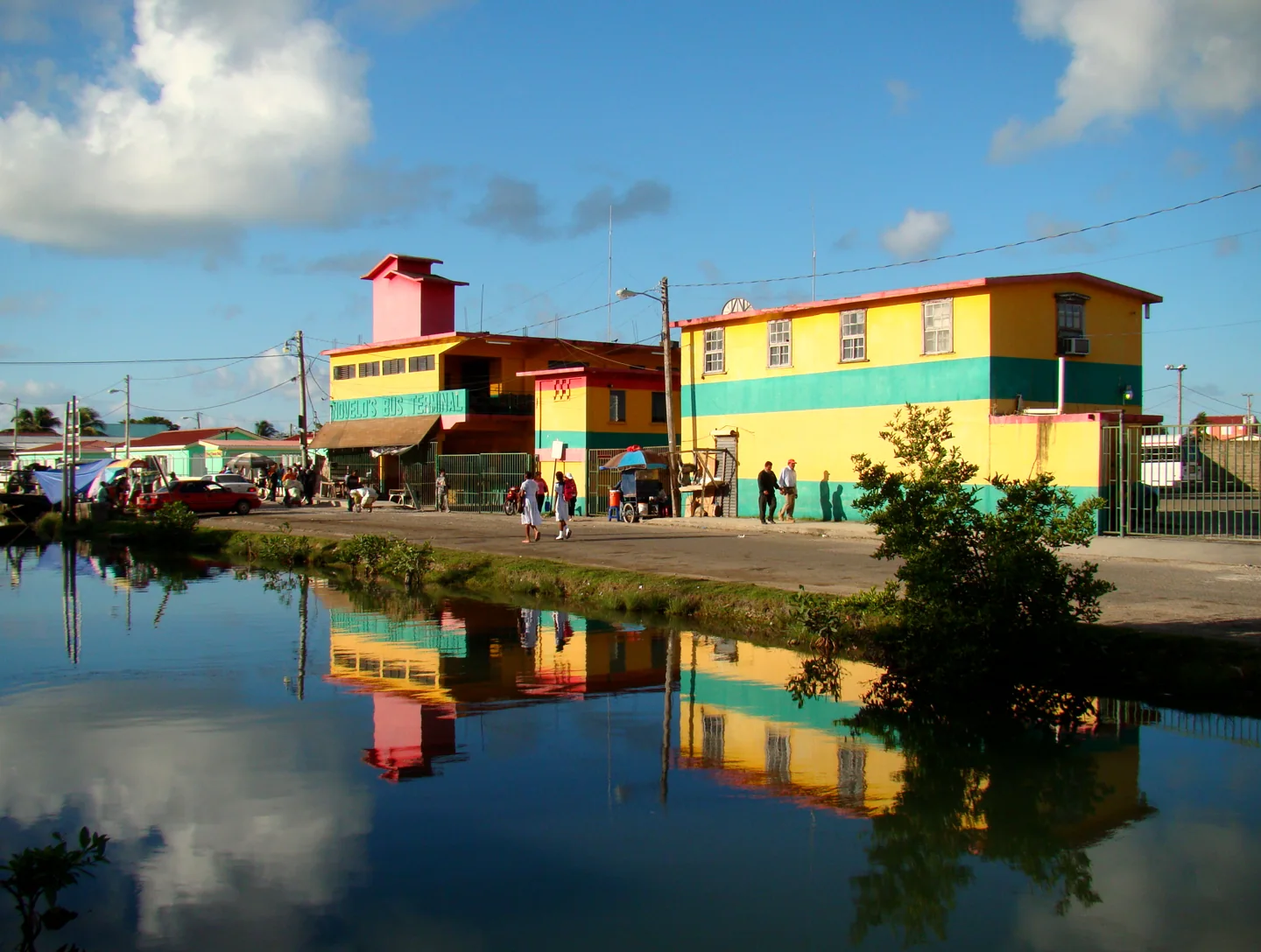 The yellow-and-green Novelo's Bus Terminal building beside water, with pedestrians outside.