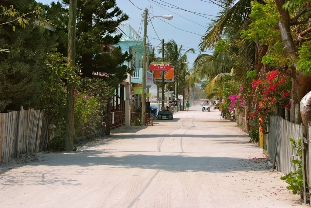 A sandy Caye Caulker street with palms, low buildings and golf carts.
