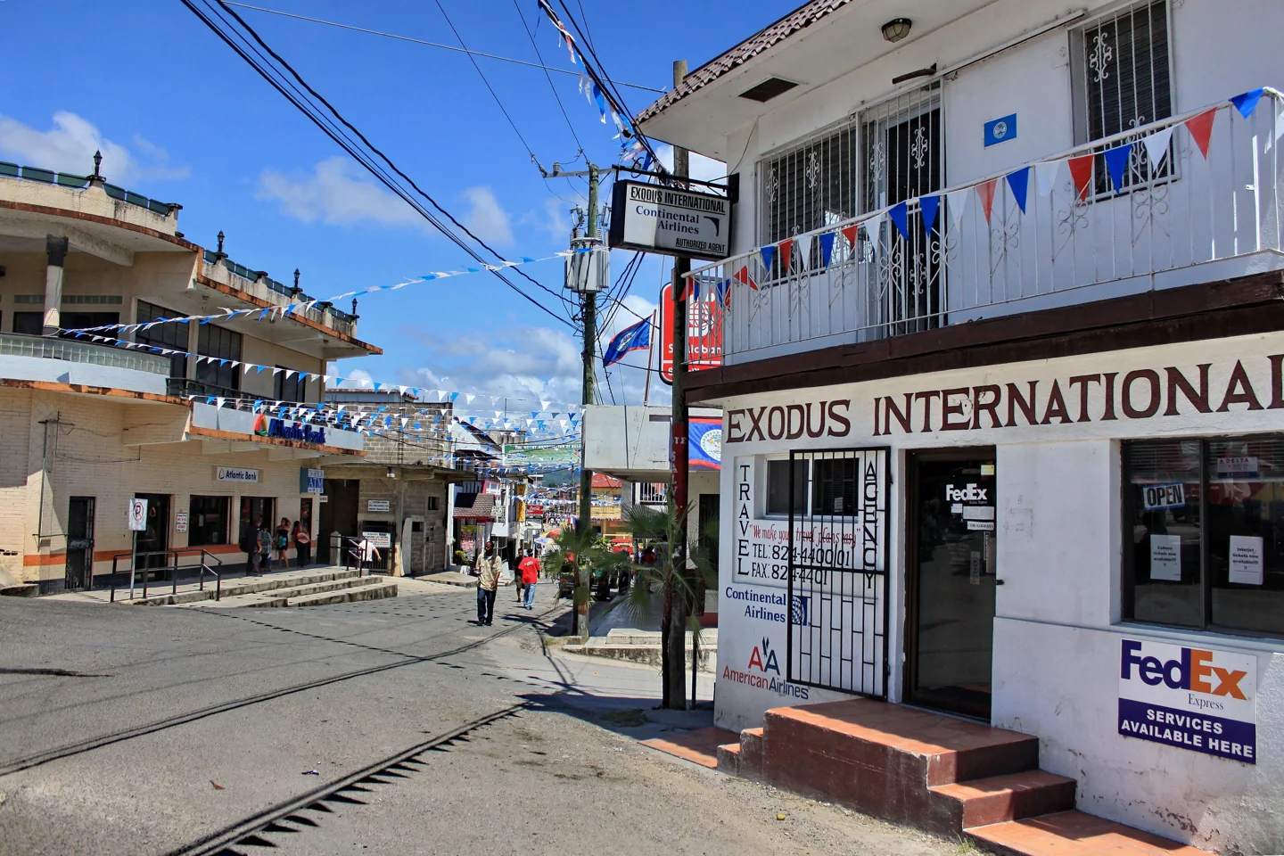 Pedestrians on a San Ignacio street lined with low-rise shops, balconies and Belize flags.
