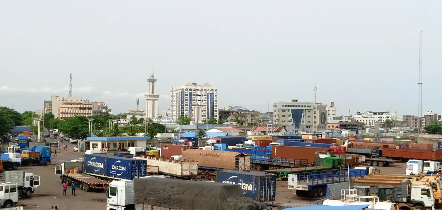 Trucks and shipping containers before city buildings and a mosque minaret in Zongo, Cotonou.