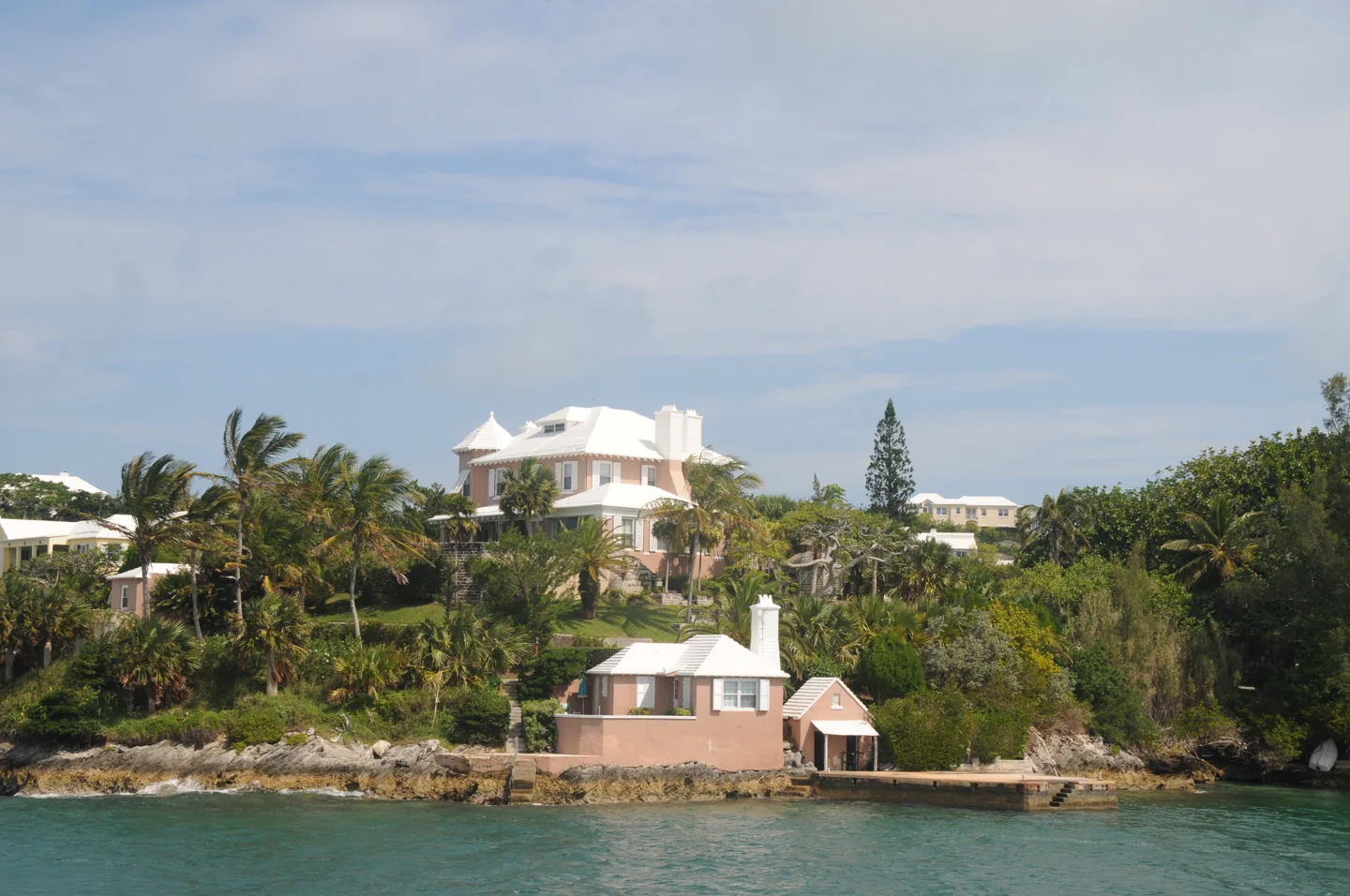 Pink house with white stepped roofs and palm trees beside Hamilton Harbour