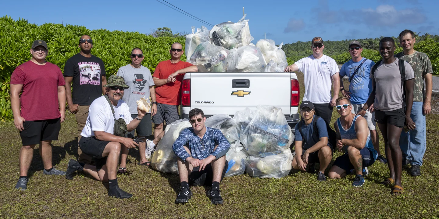 Diego Garcia personnel posing together after a beach cleanup beside palm trees