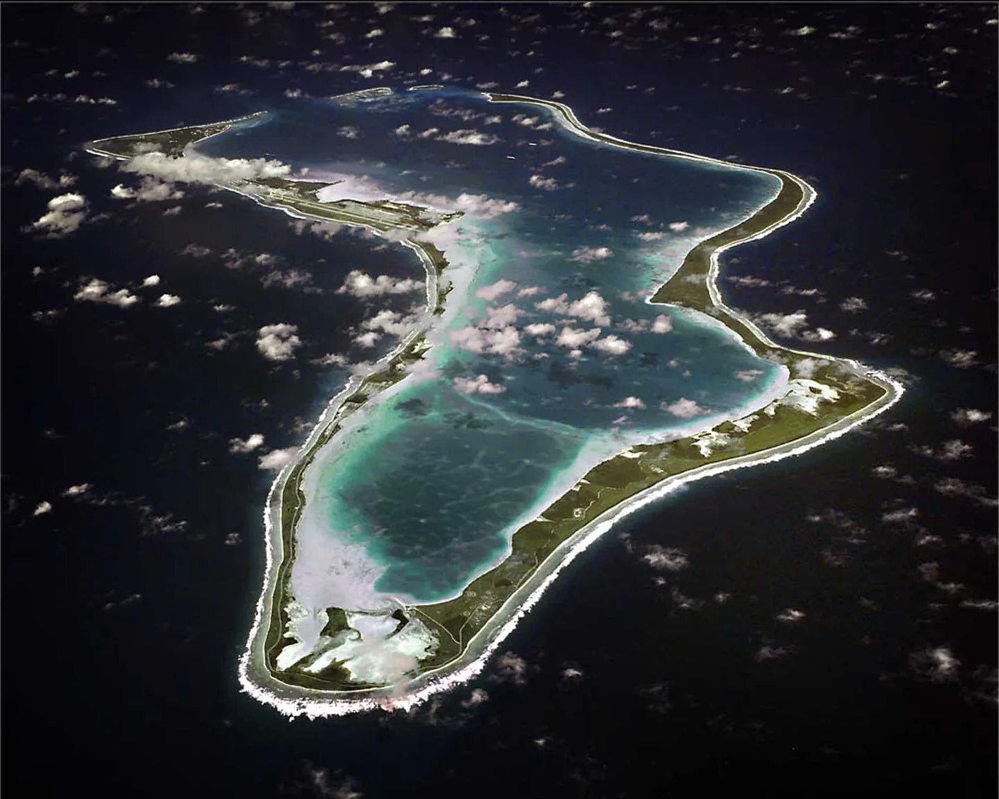 Aerial photograph of Diego Garcia's narrow palm-covered land and broad blue lagoon