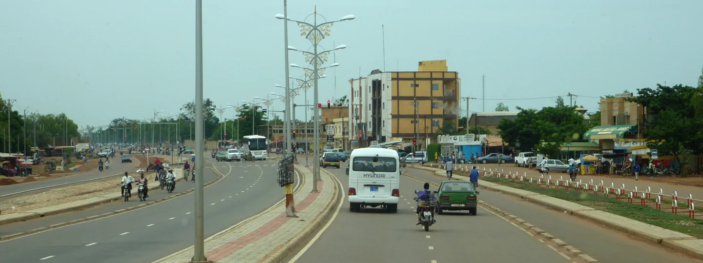 A broad avenue in Ouagadougou with buildings, traffic and roadside activity
