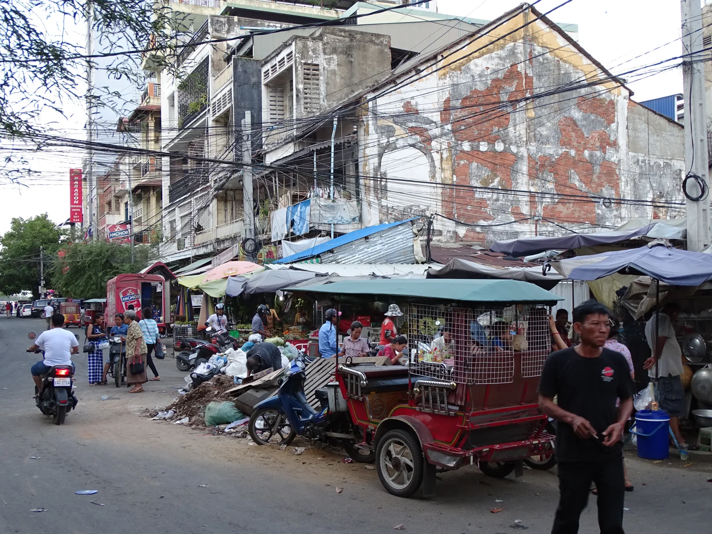 Phnom Penh street with tuk-tuks, food stalls, ordinary buildings and overhead wires