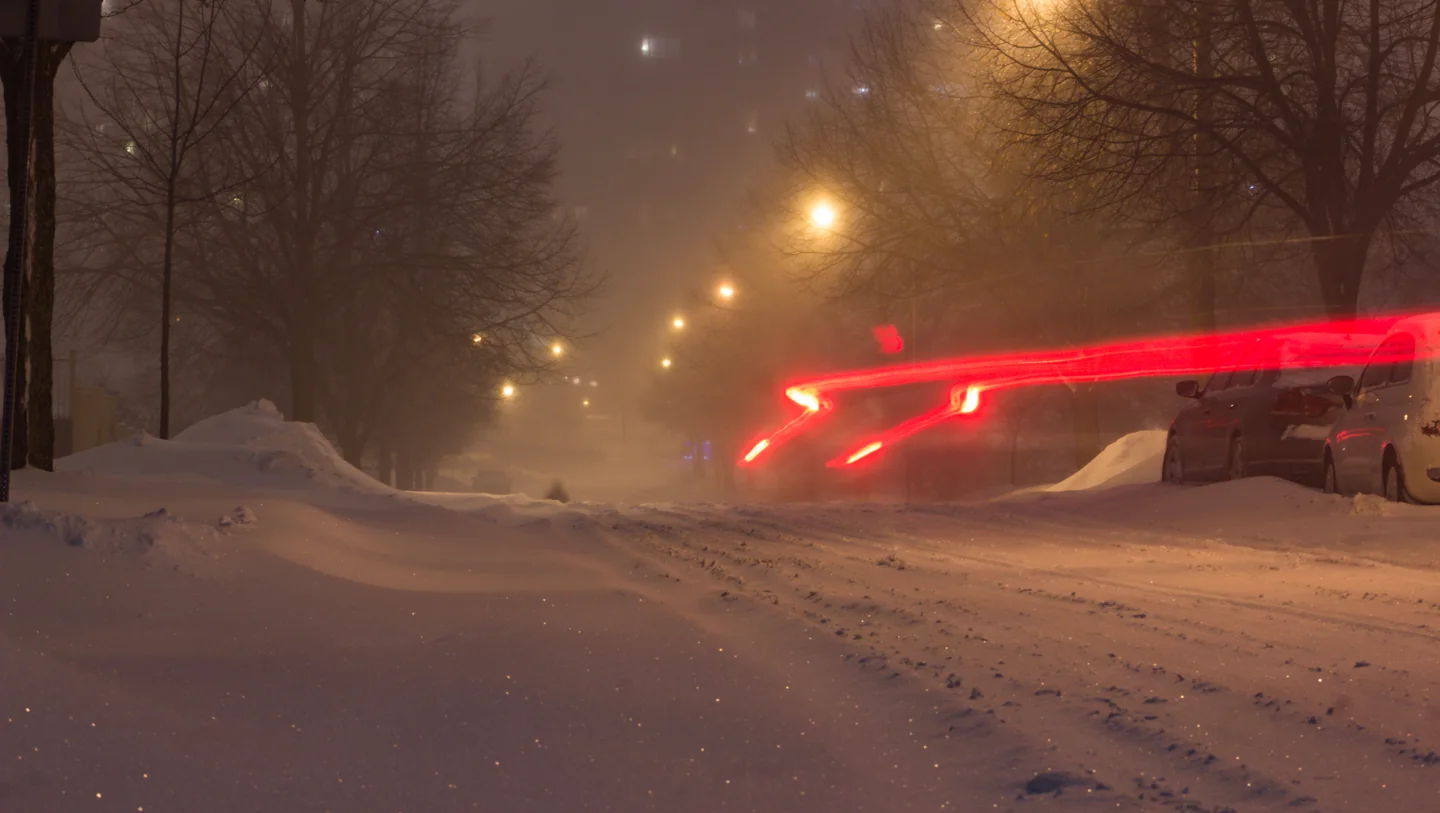 Snow-covered Toronto residential street with vehicle lights at night