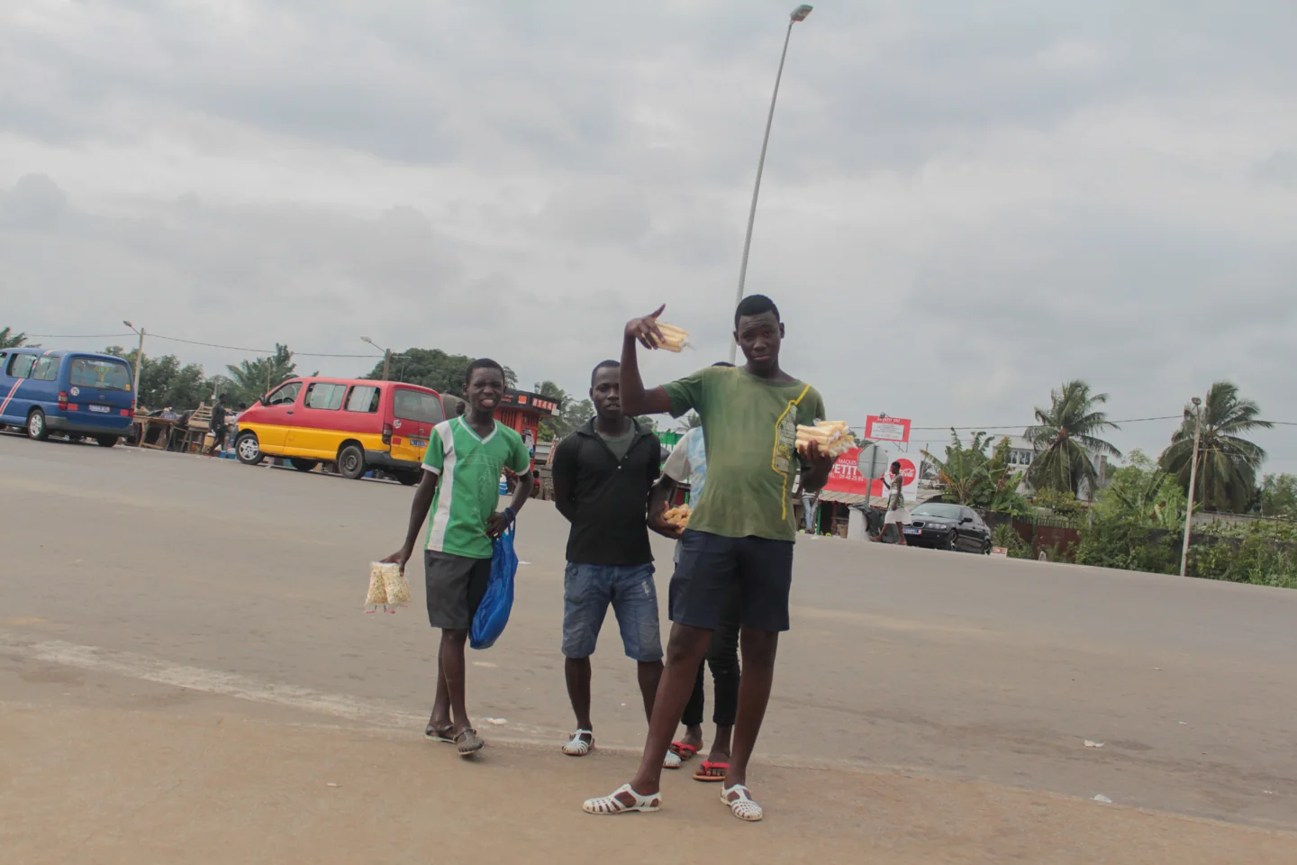 Snack vendors carrying small bags of popcorn and sugarcane on a street in Grand-Bassam