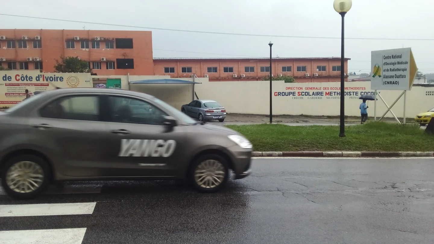 A passing car on the street outside CHU de Cocody, beside a sign for the national oncology and radiotherapy centre