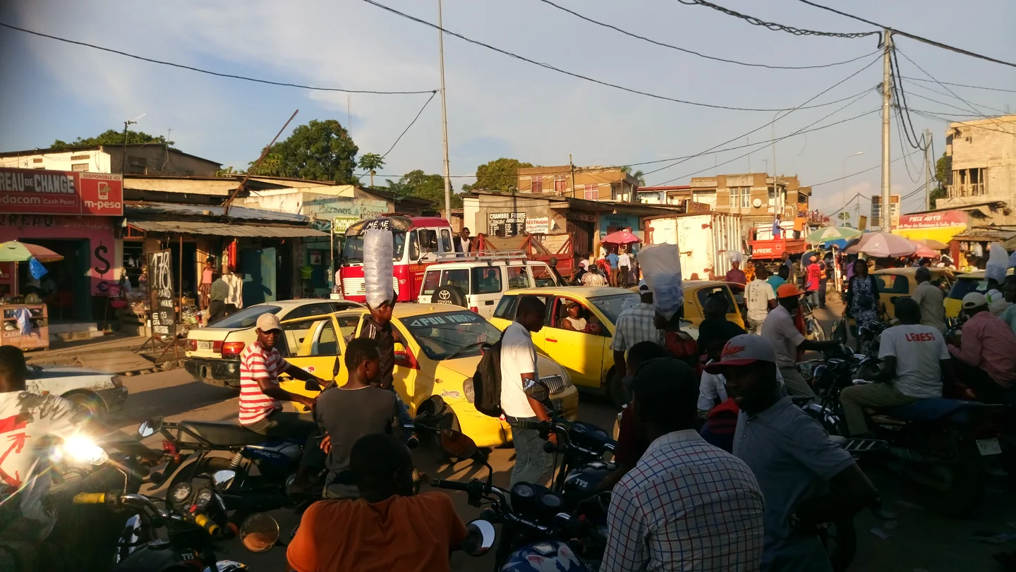 Motorcycles, yellow taxis, a minibus and pedestrians at a busy transport station in Kinshasa