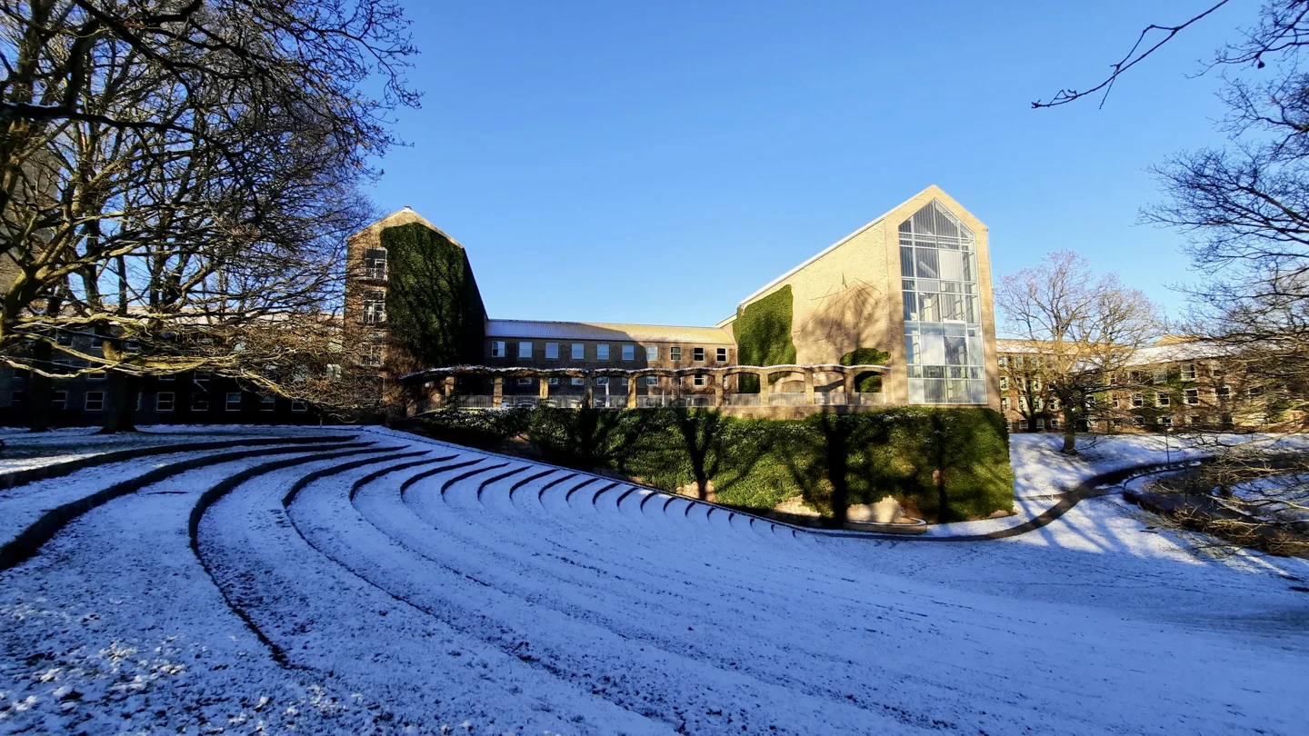 Yellow-brick Aarhus University Aula building beyond a lightly snow-covered park